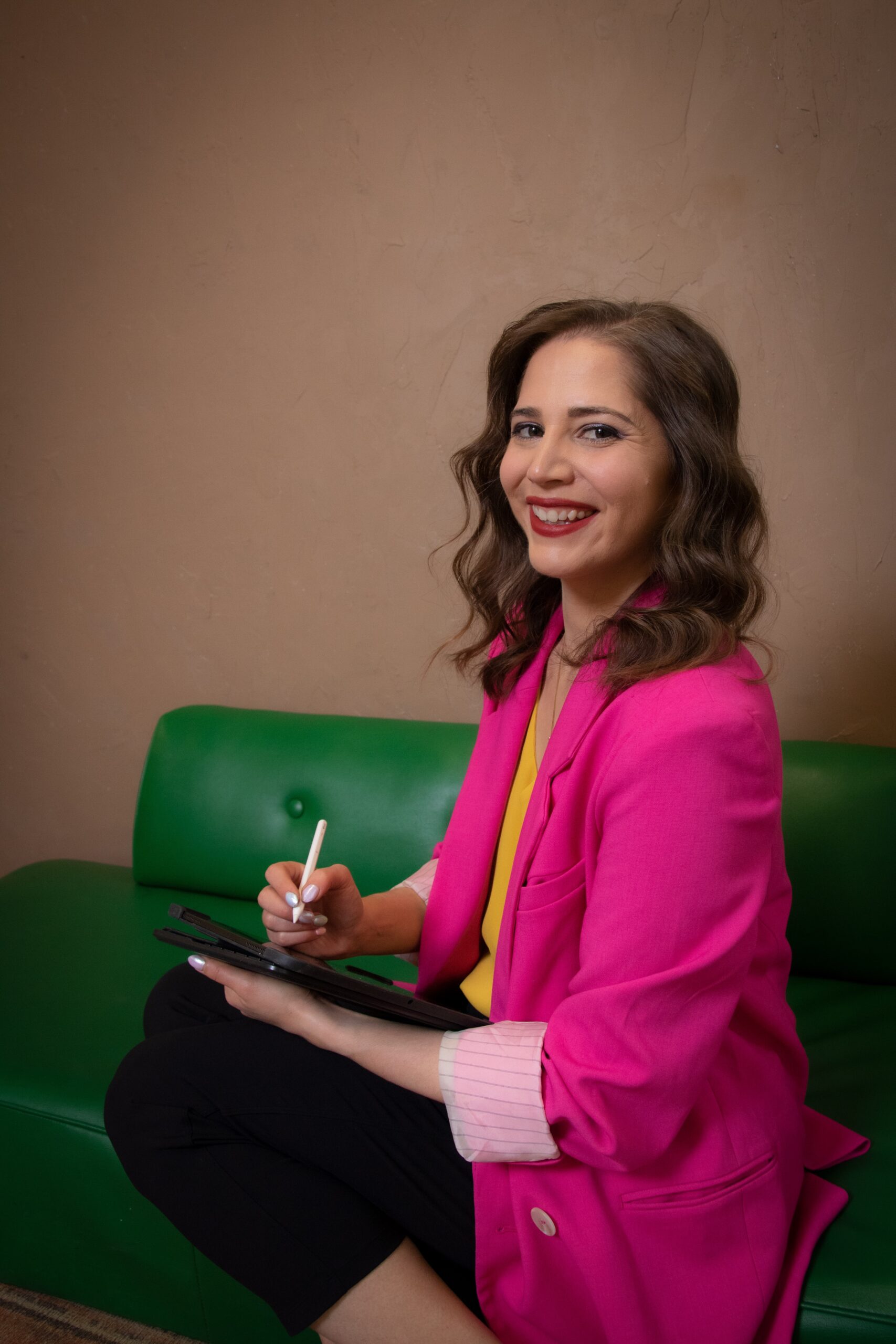 Emily Decloux holding an ipad and apple pencil sitting on a green couch wearing pink jacket. how much does a wedding planner cost in Toronto?